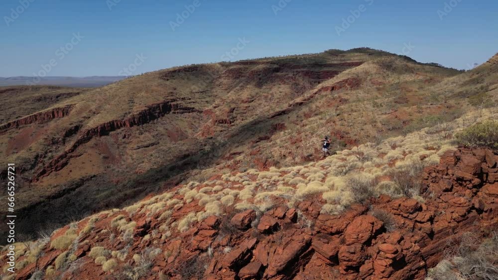 Aerial orbiting shot of active hiker on rocky trail with beautiful Australian desert landscape in background during sunlight.