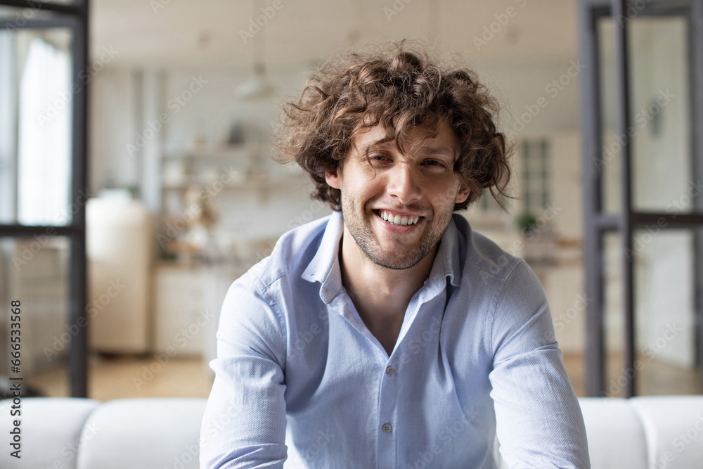 Close-up portrait of a handsome smiling man in the living room on the sofa communicating online.