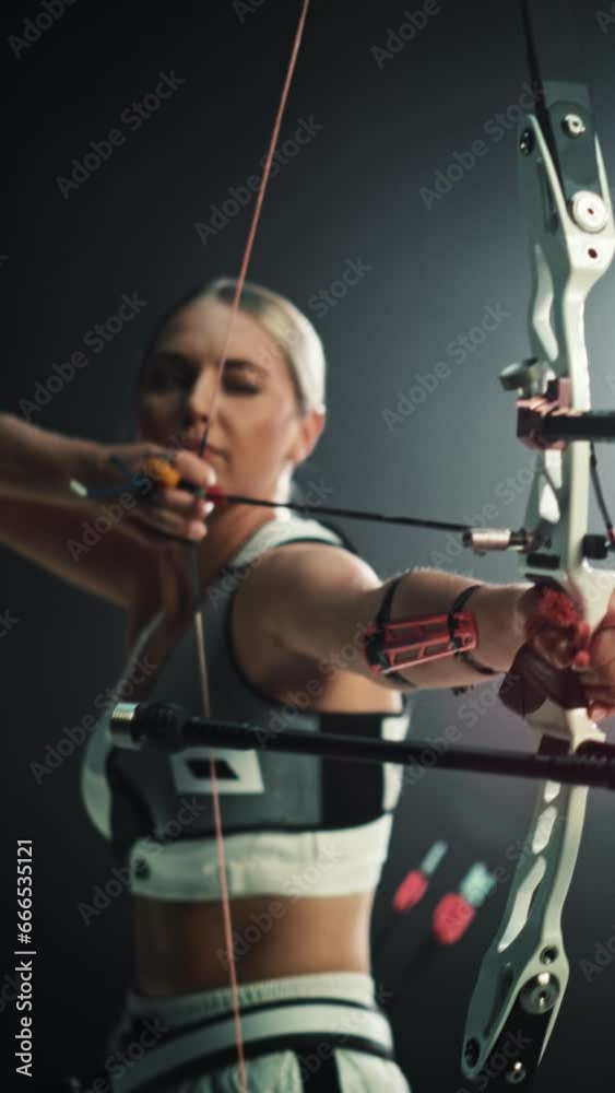 Vertical Screen: Cinematic Portrait of a Female Archer Aiming and Shooting an Arrow at a Target with a Modern Compound Bow. Strong Athlete is Fully Equipped and Protected with Chest and Arm Guards Vertical Screen: Cinematic Portrait of a Female Archer Aiming and Shooting an Arrow at a Target with a Modern Compound Bow. Strong Athlete is Fully Equipped and Protected with Chest and Arm Guards
