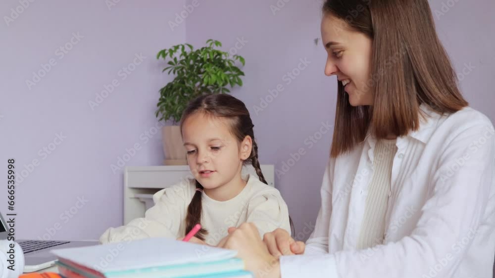Adorable positive little girl with pigtails doing schoolwork with mother help at home interior writing in copy book tutor explaining kids knowledge. Adorable positive little girl with pigtails doing schoolwork with mother help at home interior writing in copy book tutor explaining kids knowledge.
