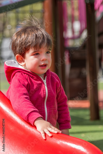 Toddler standing next to the slide on the playground in the park.