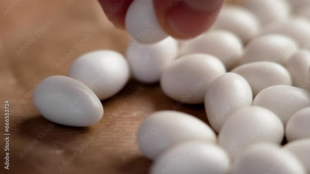 Almond nuts in white chocolate. Hand takes peanut dragee from a kraft paper. Sweet party candies Almond nuts in white chocolate. Hand takes peanut dragee from a kraft paper. Sweet party candies