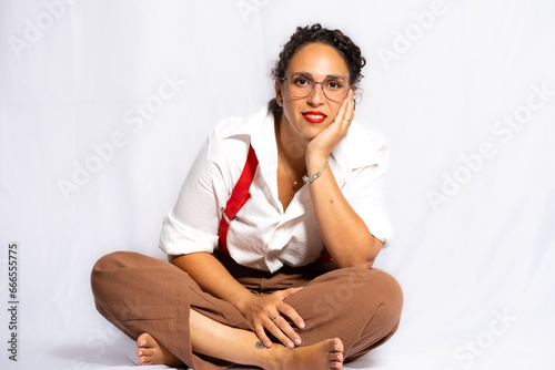 Young brunette woman with curly black hair wearing a white shirt, black lingerie, red suspenders and light brown pants