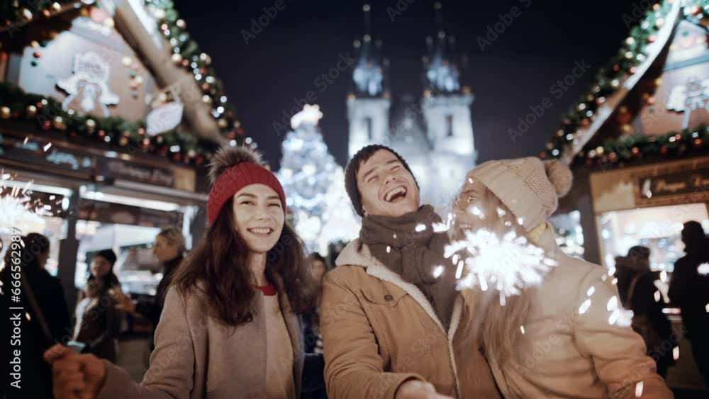 Two women and man smiling waving firework express joy happiness. Christmas holiday. Multiracial group of friends having fun with sparklers outdoor celebrating merry Christmas xmas and happy new year. Two women and man smiling waving firework express joy happiness. Christmas holiday. Multiracial group of friends having fun with sparklers outdoor celebrating merry Christmas xmas and happy new year.