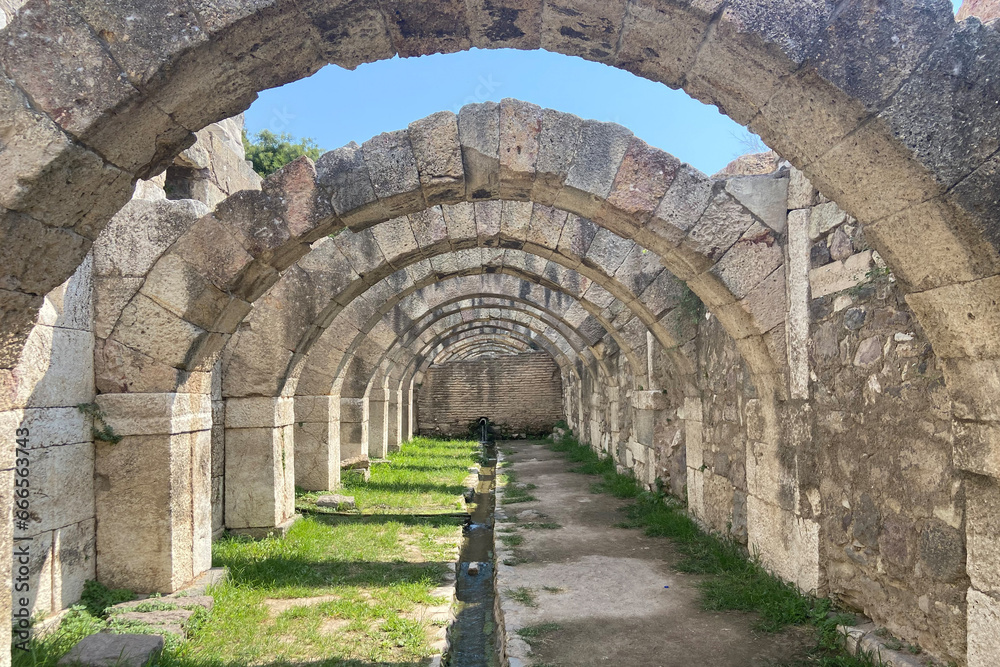 Ruins ancient city stone temple in İzmir, top arches, keystones, columns, torso statue, corridors, rooms, running fresh water between high stone wall
