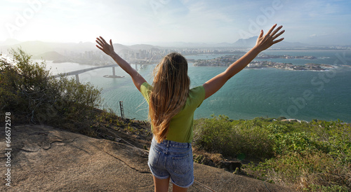 Successful woman with hands raised up on mountain peak enjoying scenery at sunset
