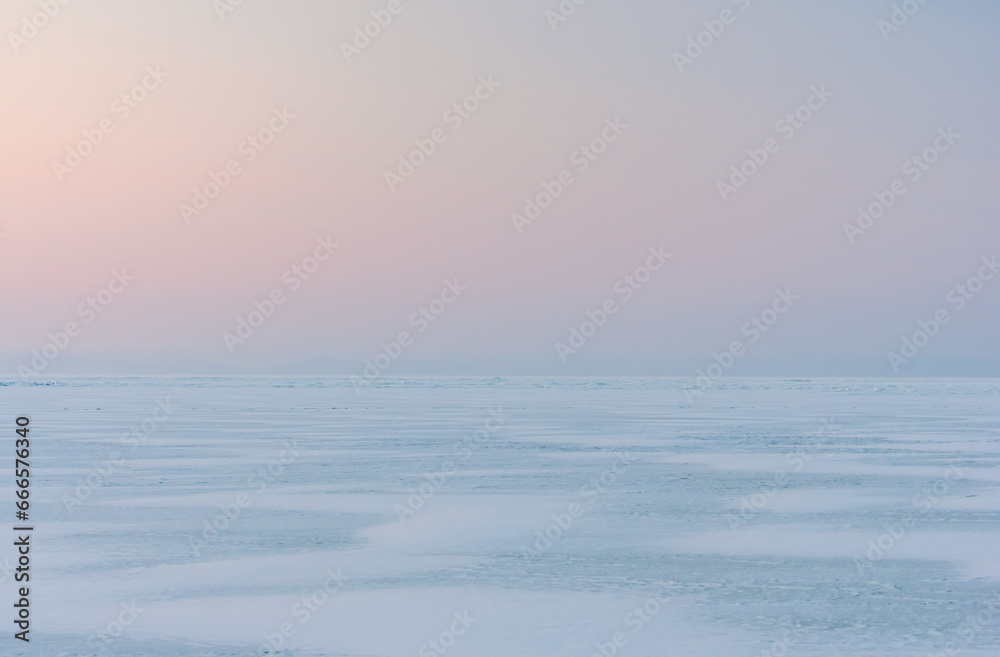 Snowdrifts on the ice surface during sunset. Winter landscape. A frozen surface of ice with snow intersected by many cracks.