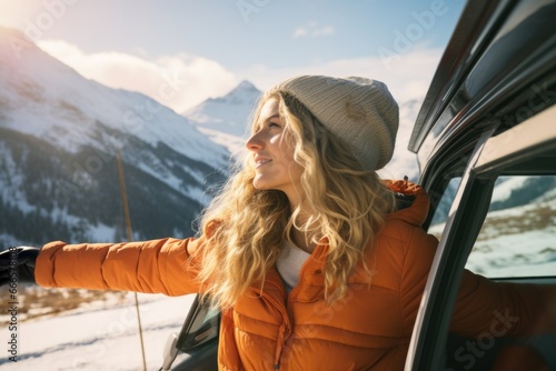 A content woman leaning on a car door, enjoying the winter mountain landscape while traveling, exploring and appreciating the beauty of the mountains.