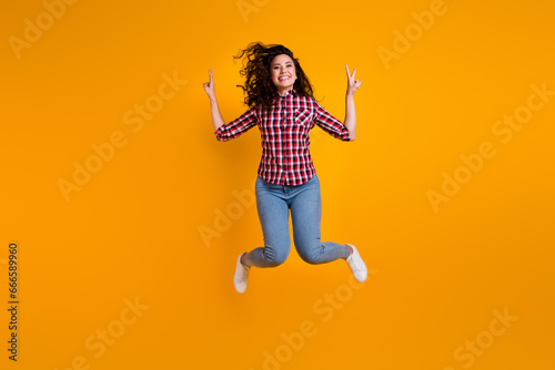 Full size photo of positive woman with wavy hairdo dressed checkered shirt flying showing v-sign symbol isolated on yellow background © deagreez