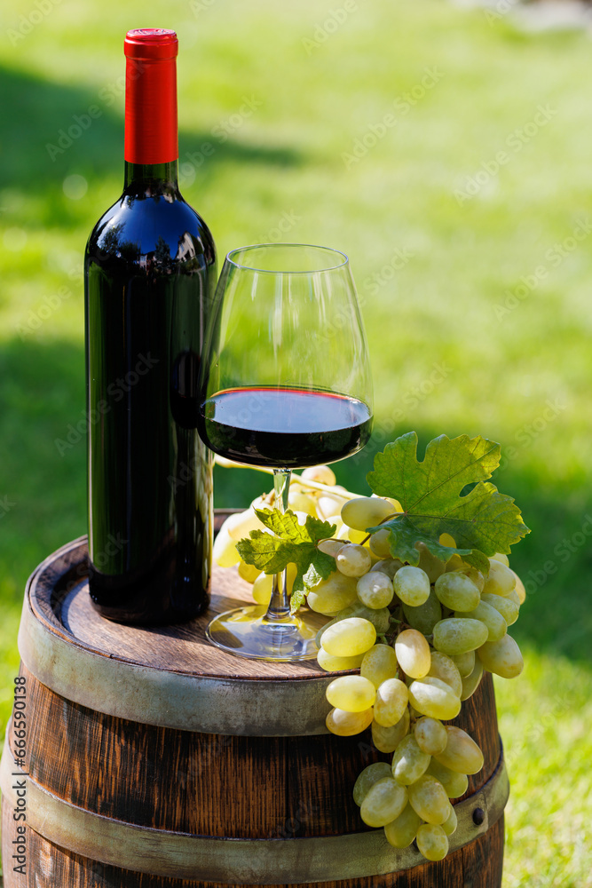 Wine bottle, red win glass and grape on barrel