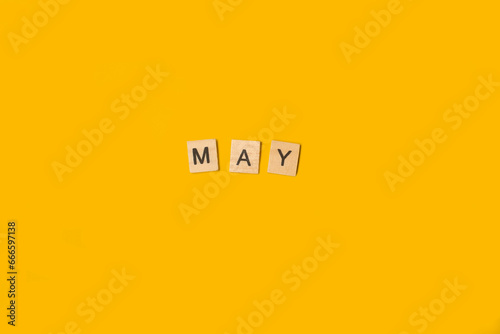 Bloques de madera formando la palabra mayo sobre un fondo amarillo liso y aislado. Vista superior. Copy space
