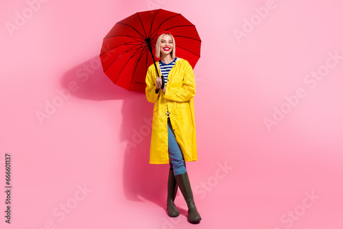 Full length photo of dreamy sweet lady wear raincoat holding umbrella walking empty space isolated pink color background