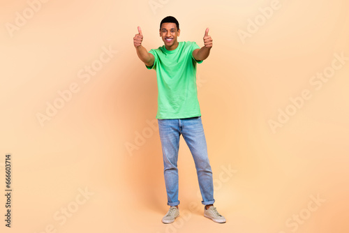 Full length photo of good mood friendly man wear stylish t-shirt jeans showing thumbs up good job isolated on beige color background