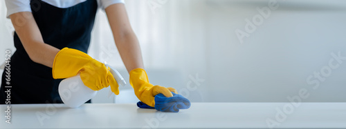 Cleaning desk surface in office with sanitizer spray, wear gloves and wipe the table with a towel, the housekeeper is cleaning the work desk for hygiene because of the Covid-19, cleaning idea.