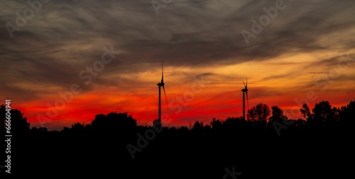 the sun rises behind the wind turbines in a red sky