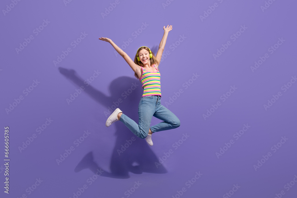 Full size photo of pretty teenager blonde girl jump raise hands excited wear trendy striped outfit isolated on purple color background