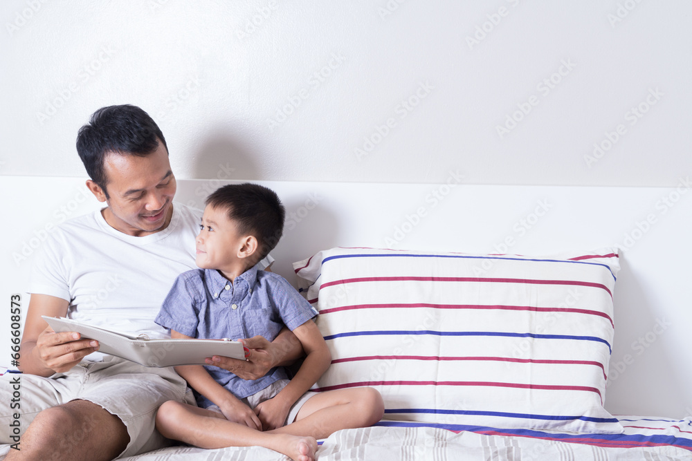 happy asian Father and son reading book together while laying on bed. happy family, father day happy asian Father and son reading book together while laying on bed. happy family, father day