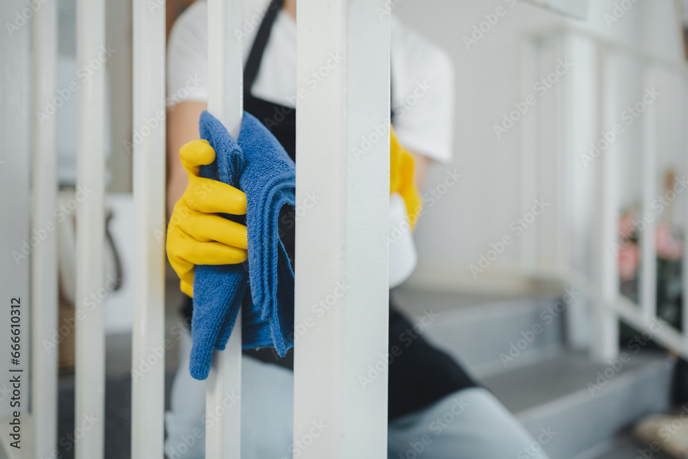 Housekeeper cleaning the furniture at home, Wear an apron and rubber gloves to protect against cleaning chemicals, female wiping down stairs with cleaning spray, cleaning idea. - obrazy, fototapety, plakaty 