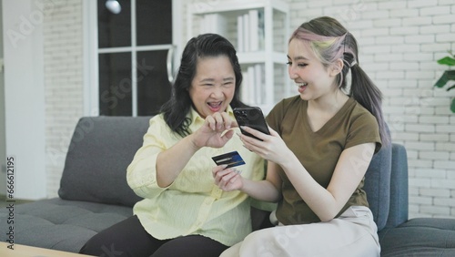 young asian daughter use smartphone with older mother enjoy shopping online on internet website together in living room at home