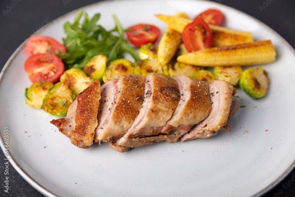 Grilled duck breast fillet with Brussels sprouts, mini corn, cherry tomatoes and arugula. Traditional Mediterranean cuisine. Selective focus, close-up.