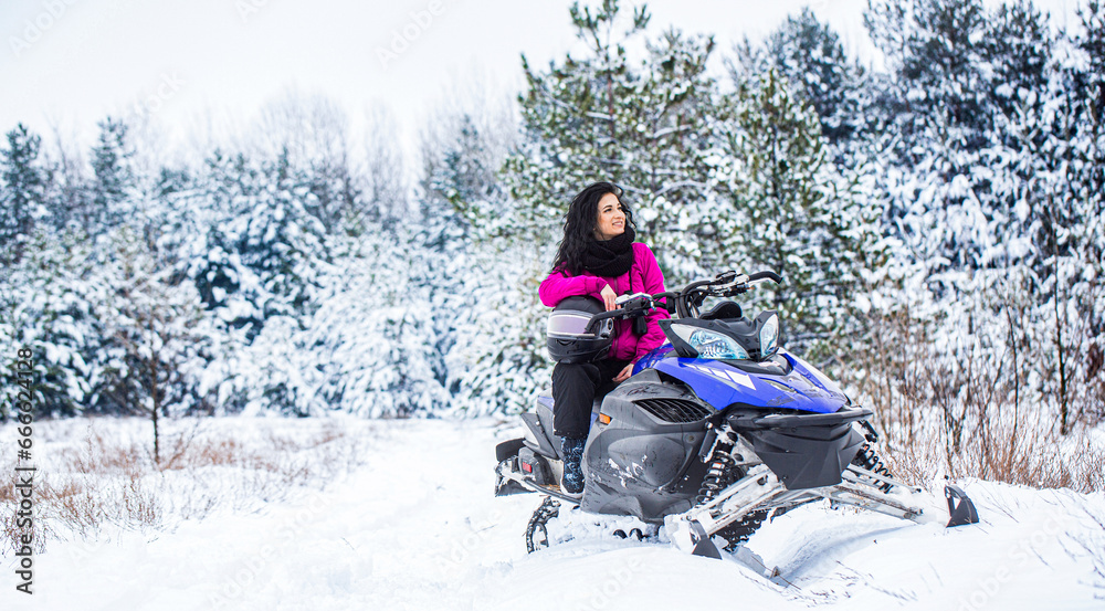 Girl on a sports snowmobile in a mountain forest. Athlete rides a snowmobile in the mountains. Snowmobile in snow. Concept winter sports. Woman is riding snowmobile in mountains