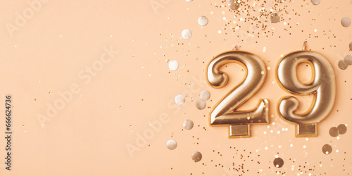 29 years celebration. Greeting banner. Gold candles in the form of number twenty nine on peach background with confetti. photo