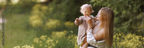 A young european woman in casual, comfortable beige clothes holding a small child in her arms in the park. Happy moments of life, family vacation in nature with copy space. Banner with copy space.