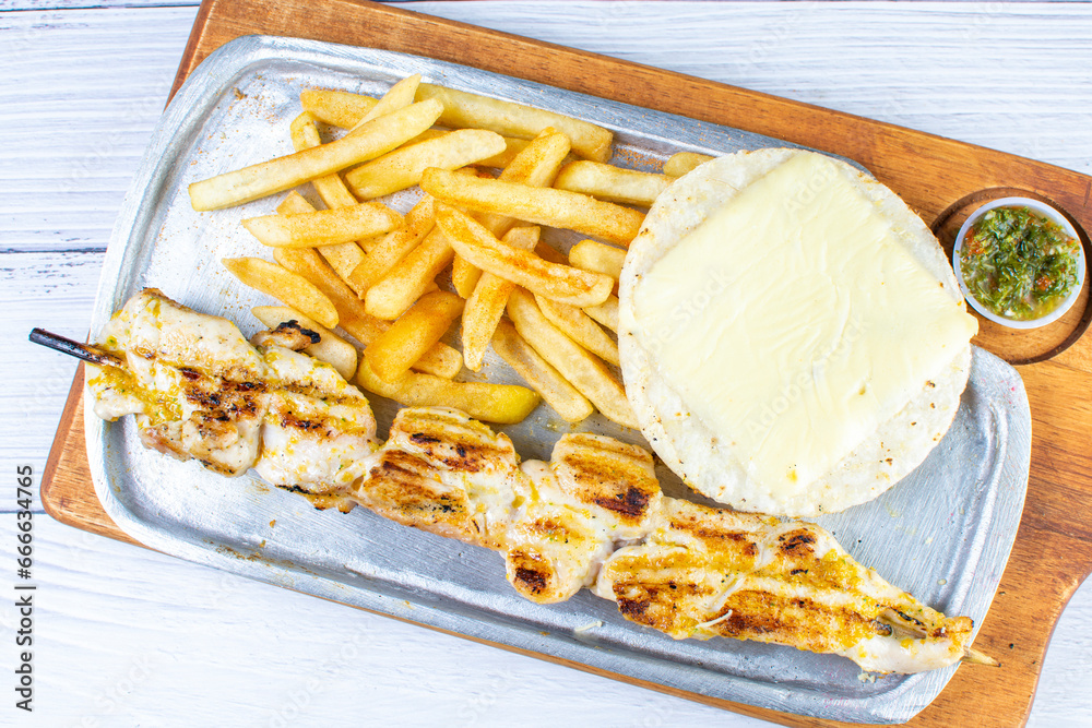 Grilled chicken skewer tray, accompanied by arepa with cheese, French fries and chimichurri