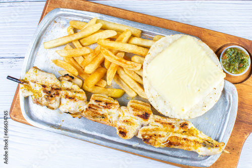 Obraz na płótnie Grilled chicken skewer tray, accompanied by arepa with cheese, French fries and chimichurri w salonie