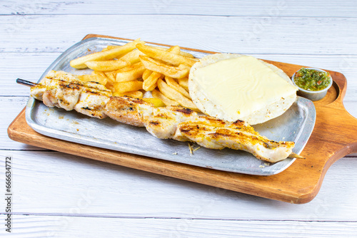 Obraz na płótnie Grilled chicken skewer tray, accompanied by arepa with cheese, French fries and chimichurri w salonie