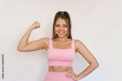 Young attractive fit athlete blonde woman with flat abs in a pink sportswear showing bicep demonstrating strength isolated on a white background. Fitness, workout. Healthy lifestyle, wellness, sports