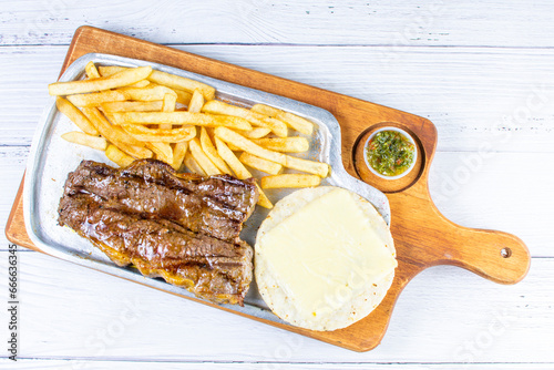 Tray of roasted haunch tip, accompanied by arepa with cheese, French fries and chimichurri
