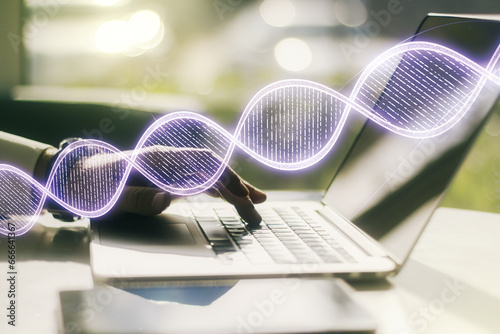 Double exposure of creative DNA hologram and hands typing on laptop on background. Bio Engineering and DNA Research concept