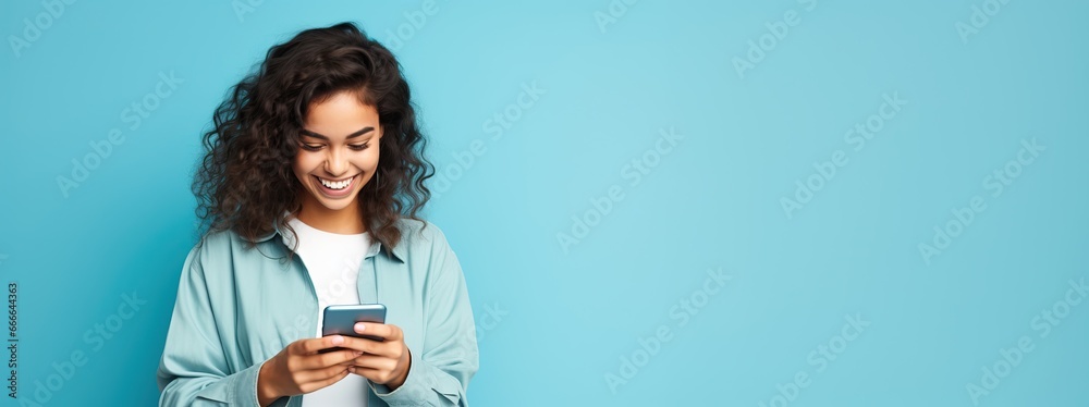 Portrait of a surprised amazed smiling casual curly student woman holding a smartphone isolated over blue background. Portrait of a surprised amazed smiling casual curly student woman holding a smartphone isolated over blue background.