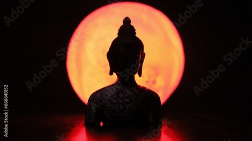 Gautam Buddha silhouette in front of orange moon background in the dark- creating a serene scene 