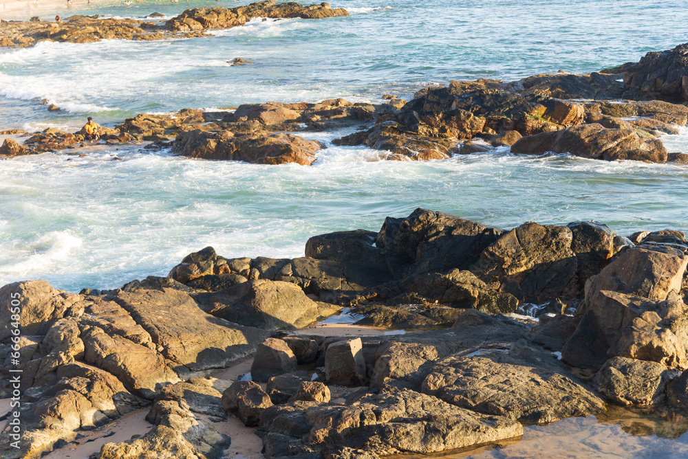 Sea waves lapping gently on the dark rocks of the beach.