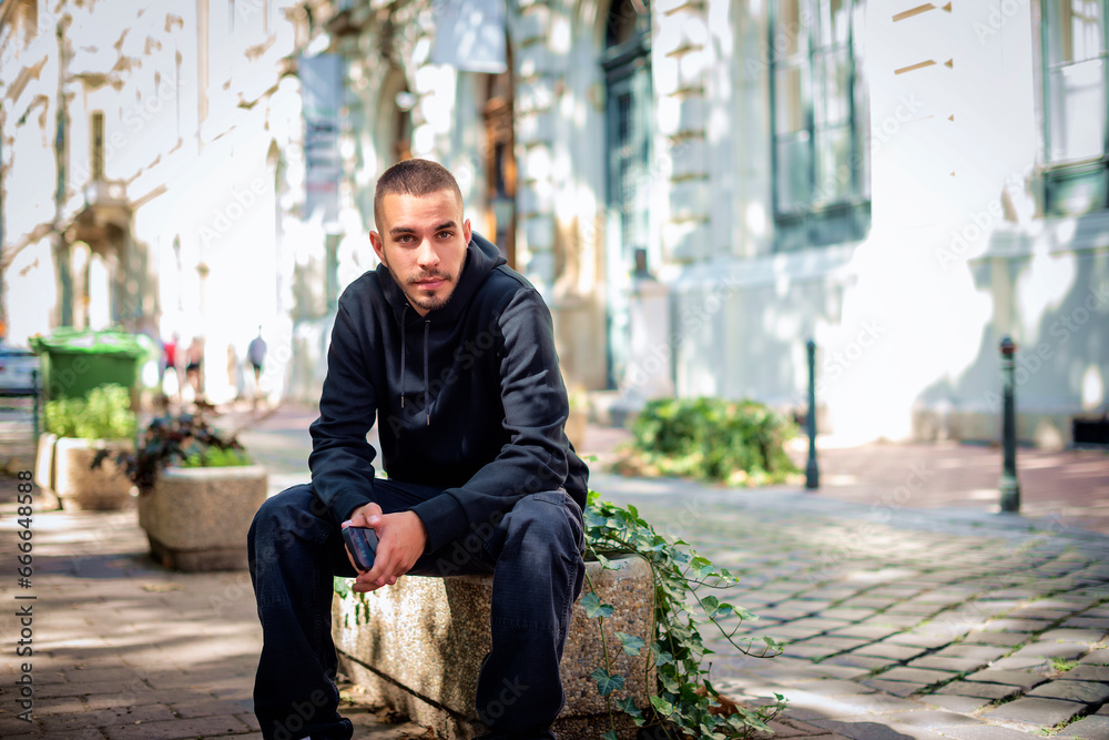 Portait of a generation Z man wearing hoodie and sitting on the city street Portait of a generation Z man wearing hoodie and sitting on the city street