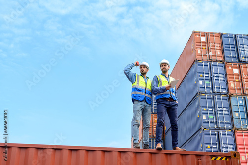 Container operator wearing white helmet and reflection shirt and holding tablet doing routine inspection while working in container yards. Logistics and shipping concept