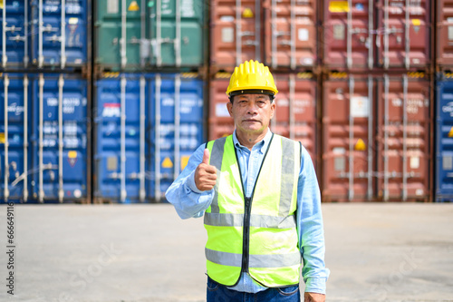 Portrait of Logistic engineer worker man standing in shipping container yard looking and thumb up to the camera. engineering at container cargo site, industrial container cargo freight ship