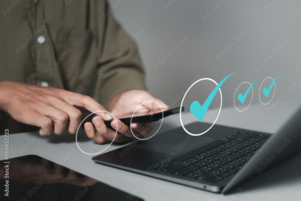 Checklist concept, Man using smartphone and laptop to ticks checklist and takes online assessment survey test for approve business project. Quality assurance and ISO guarantee. Checklist concept, Man using smartphone and laptop to ticks checklist and takes online assessment survey test for approve business project. Quality assurance and ISO guarantee.