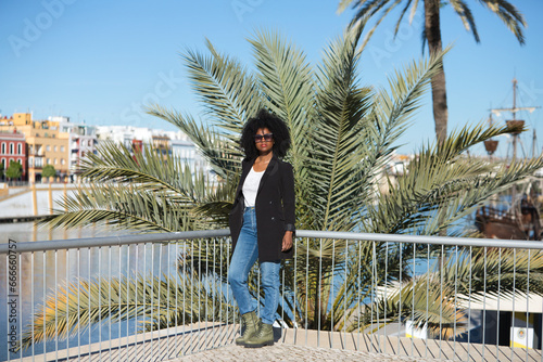 Young beautiful black woman with afro hair dressed in casual clothes and leaning on the railing while enjoying her holidays in seville  spain. In the background the river and the flamenco quarter.