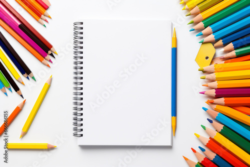 Colored pencils and notebook on white background. View from above