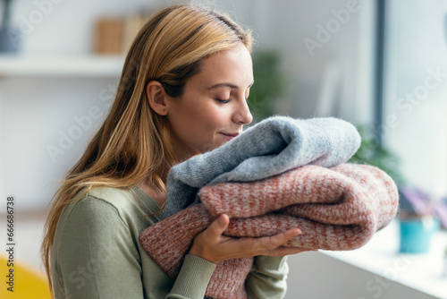 Fotografía Beautiful young woman holding and smelling clean clothes at home.