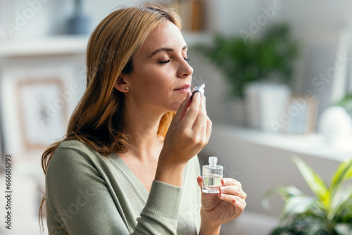 Canvastavla Beautiful woman girl holding a bottle of essential oil while testing it sitting on a couch at home