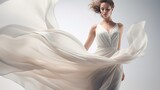 A fashion model is seen flying in the wind over a light gray background while wearing a long silk gown with chiffon fabric that resembles a cloud in a creative pure white dress.