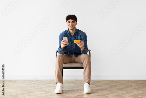 Arab guy shopping with phone and credit card sitting indoor