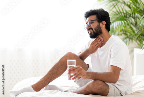 Sick indian man suffering throat ache while sitting on bed at home photo