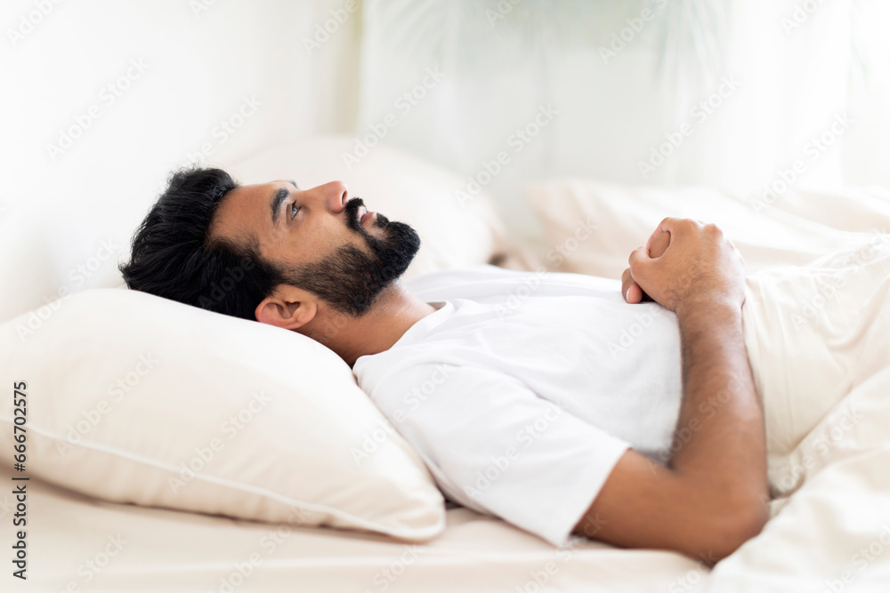 Insomnia Concept. Depressed indian man unable to sleep, lying in bed alone Insomnia Concept. Depressed indian man unable to sleep, lying in bed alone