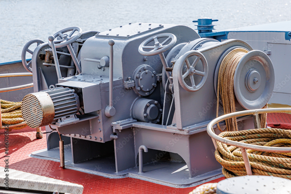 Closeup of a large ship control mooring station with levers, steering wheels, anchor windlass machine and heavy duty winches with tow rope on bow of a cargo ship, water in background blurred - obrazy, fototapety, plakaty 
