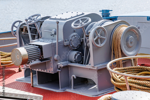 Closeup of a large ship control mooring station with levers, steering wheels, anchor windlass machine and heavy duty winches with tow rope on bow of a cargo ship, water in background blurred photo